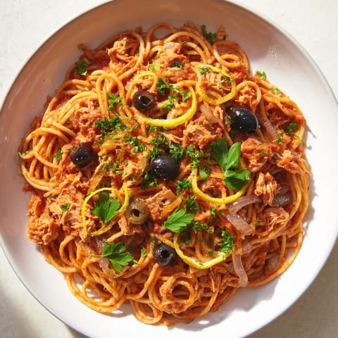Savor the flavors of this pasta with tuna, olives, and capers, with bright red sauce and flaky tuna.