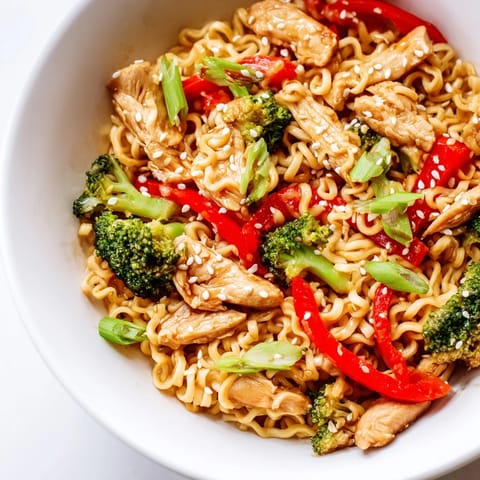Close-up of Spicy Ramen Stir-Fry in a bowl, steam rising, garnished with green onions and toasted sesame seeds for a delicious finish.  